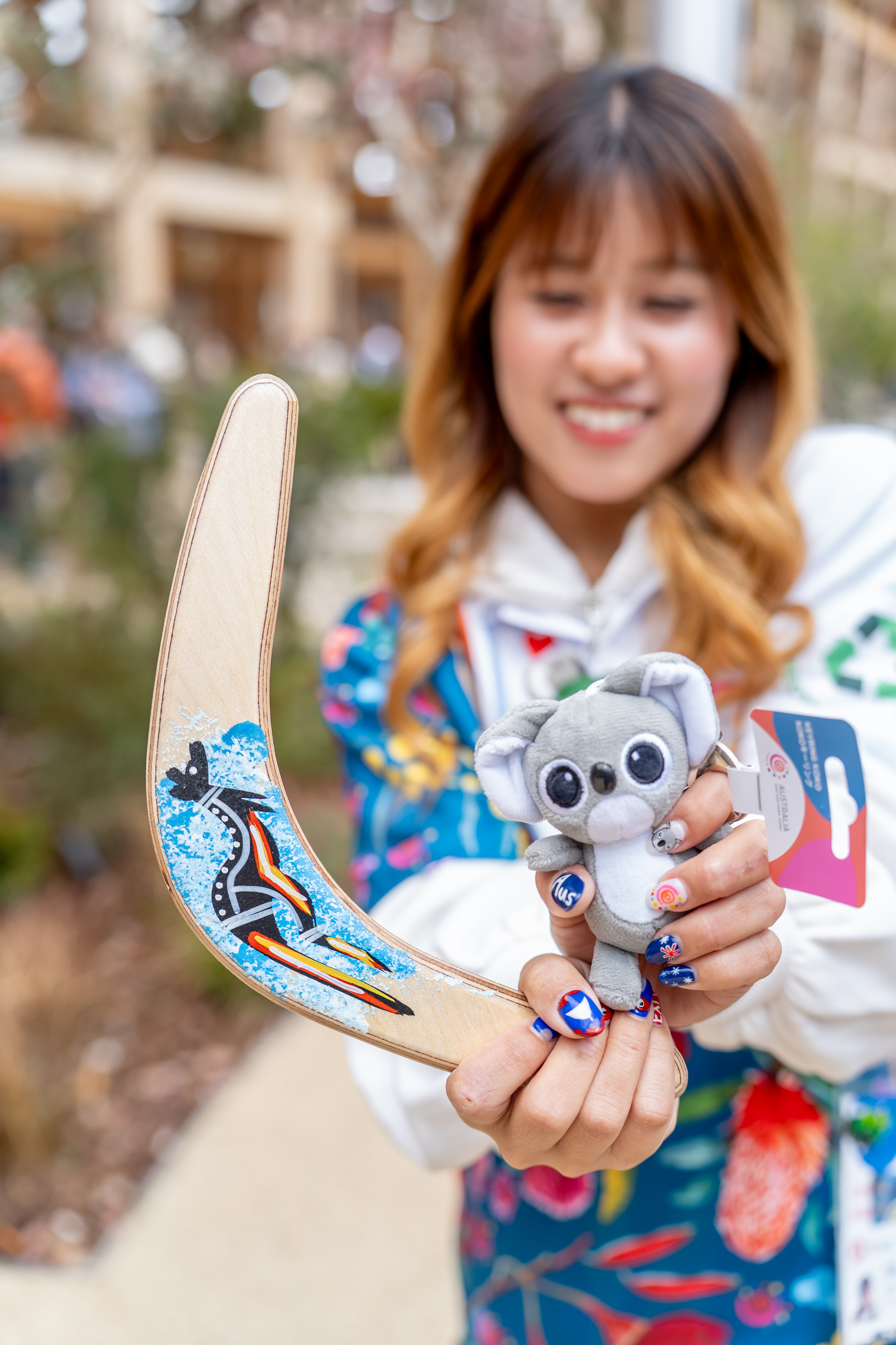 An Australia Pavilion staff member holding a Koko the Koala mini plush keyring and a painted boomerang
